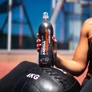Sportos, szabadtéri környezetben egy medicin labdán tartja egy női kéz az Absolute Live Mega L-karnitin sportitalt